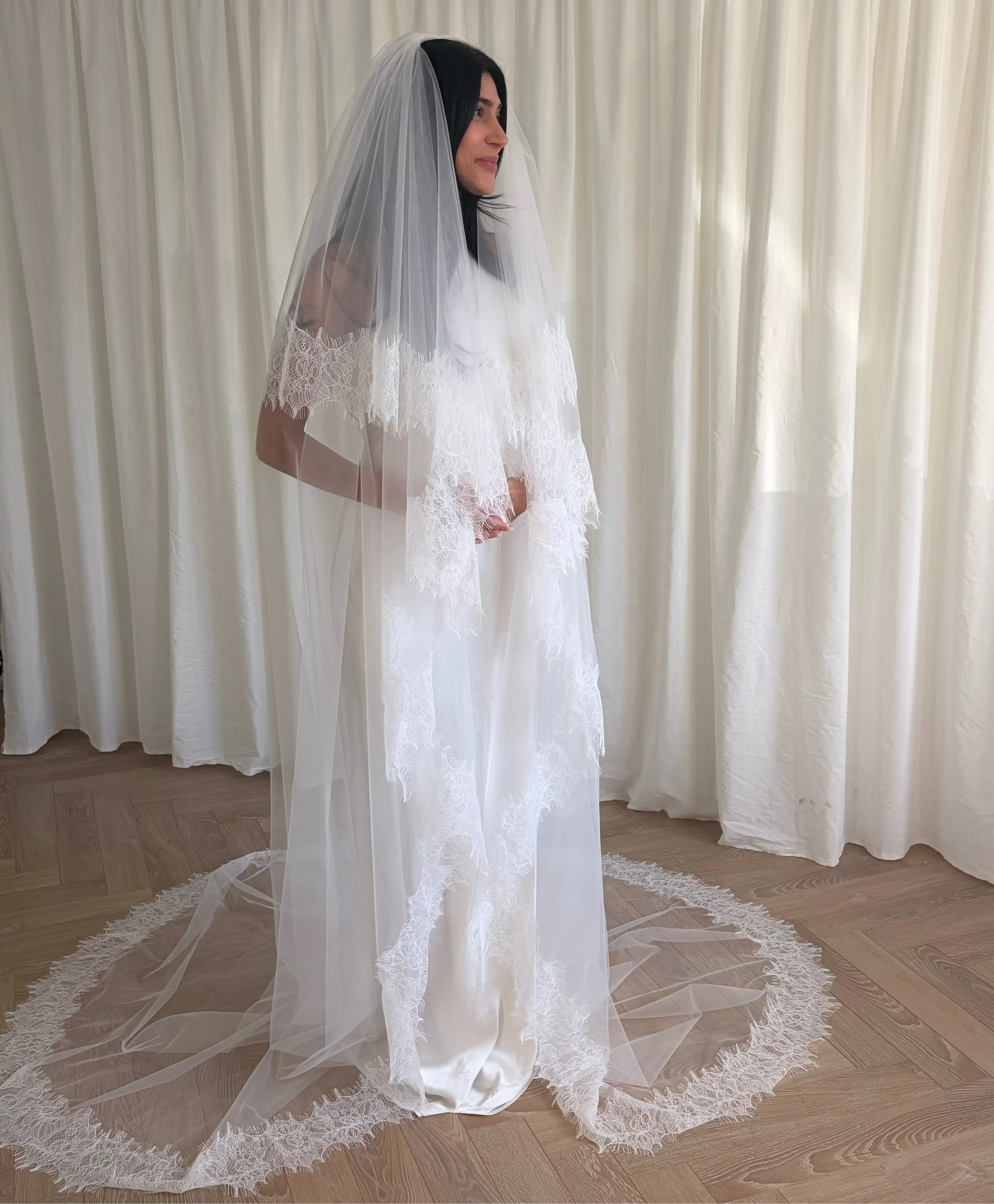 This cathedral-length lace trim blusher wedding veil flows gracefully behind the bride, made from soft, lightweight tulle and finished with intricate lace trim. Ideal for traditional or formal weddings, it creates a striking, romantic silhouette and complements any bridal gown with elegance and sophistication.