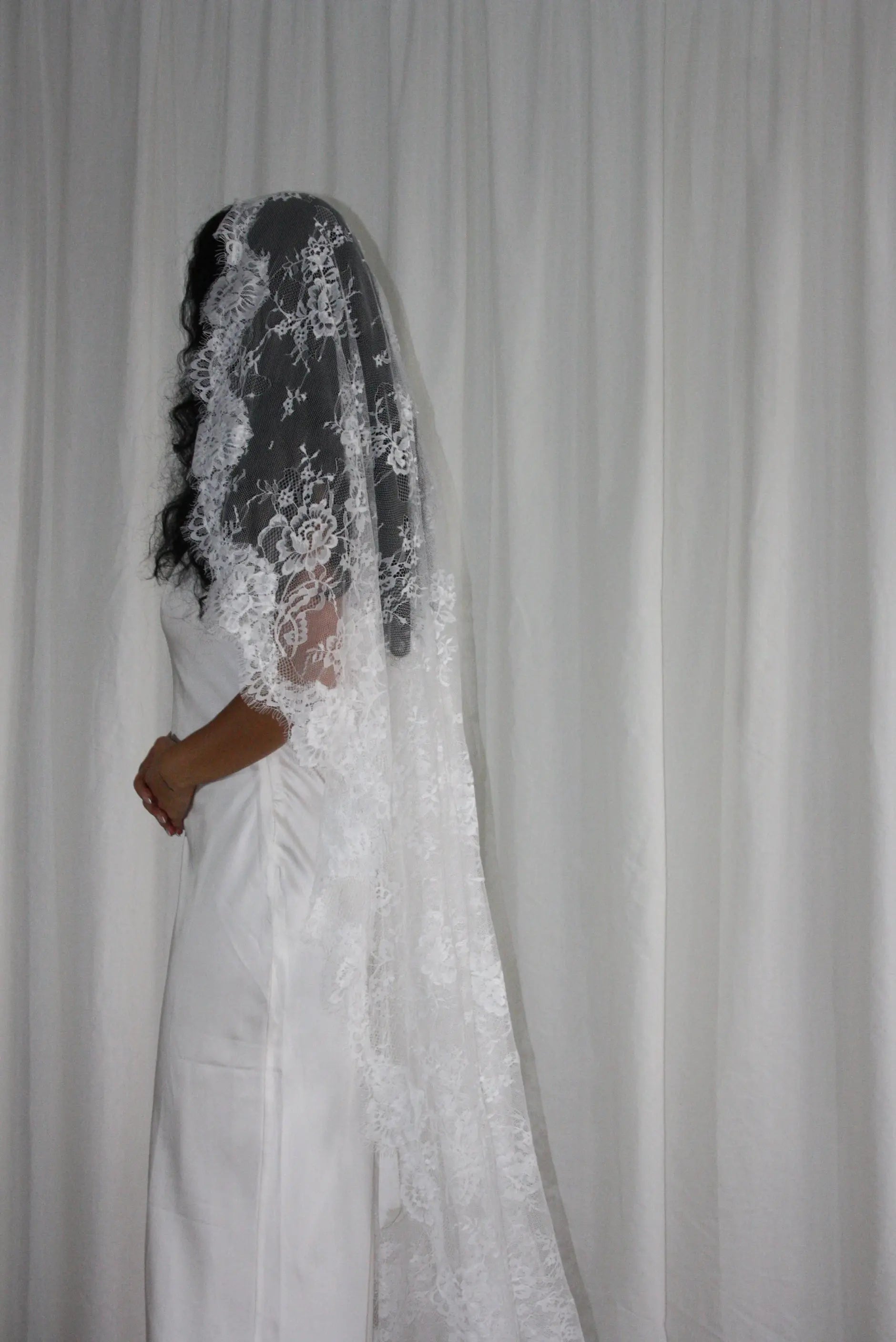 The Mantilla-Style Chantilly Rose Full Lace Veil is a cathedral-length bridal statement piece, designed for timeless elegance. Made from soft, lightweight tulle, it features intricate Chantilly rose lace that frames the veil completely, creating a delicate, romantic finish. The veil drapes beautifully straight to the ground, evoking a graceful, ethereal silhouette.This a vintage take on spanish style mantilla veil.